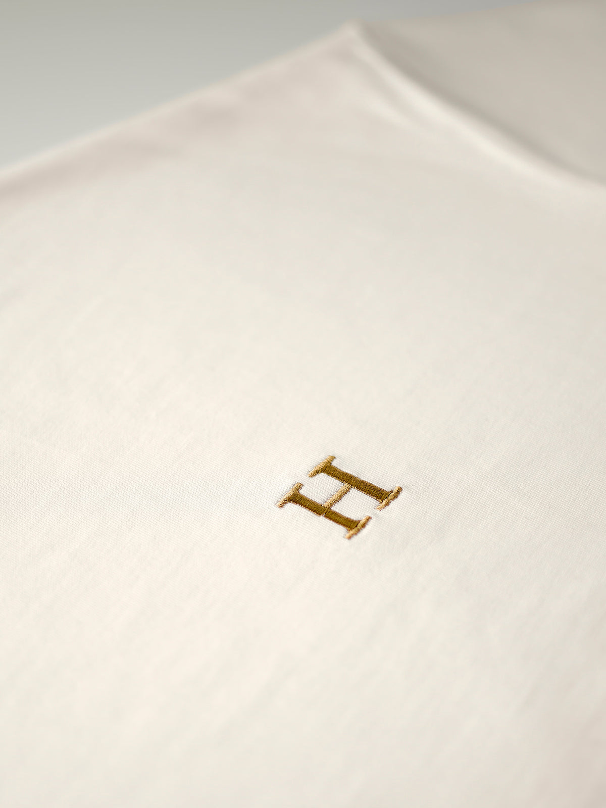 Close-up van de goud geborduurde H op het creme 240 gsm katoen